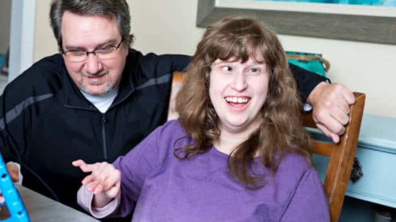 Father assists his autistic daughter with her classwork while using digital tablet at home